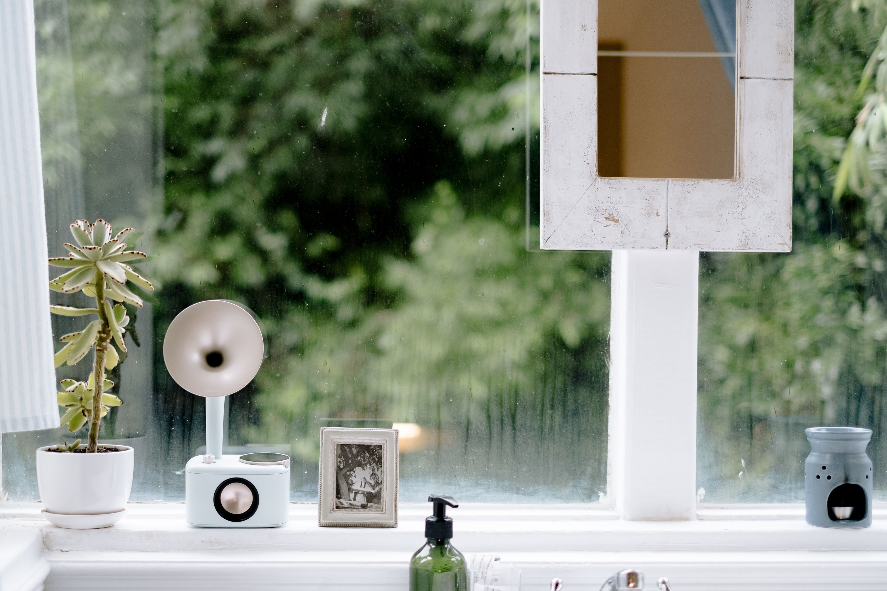 Parapet z rośliną, lampą, ramką na zdjęcia i dyfuzorem olejków eterycznych. Zielone drzewa w tle.