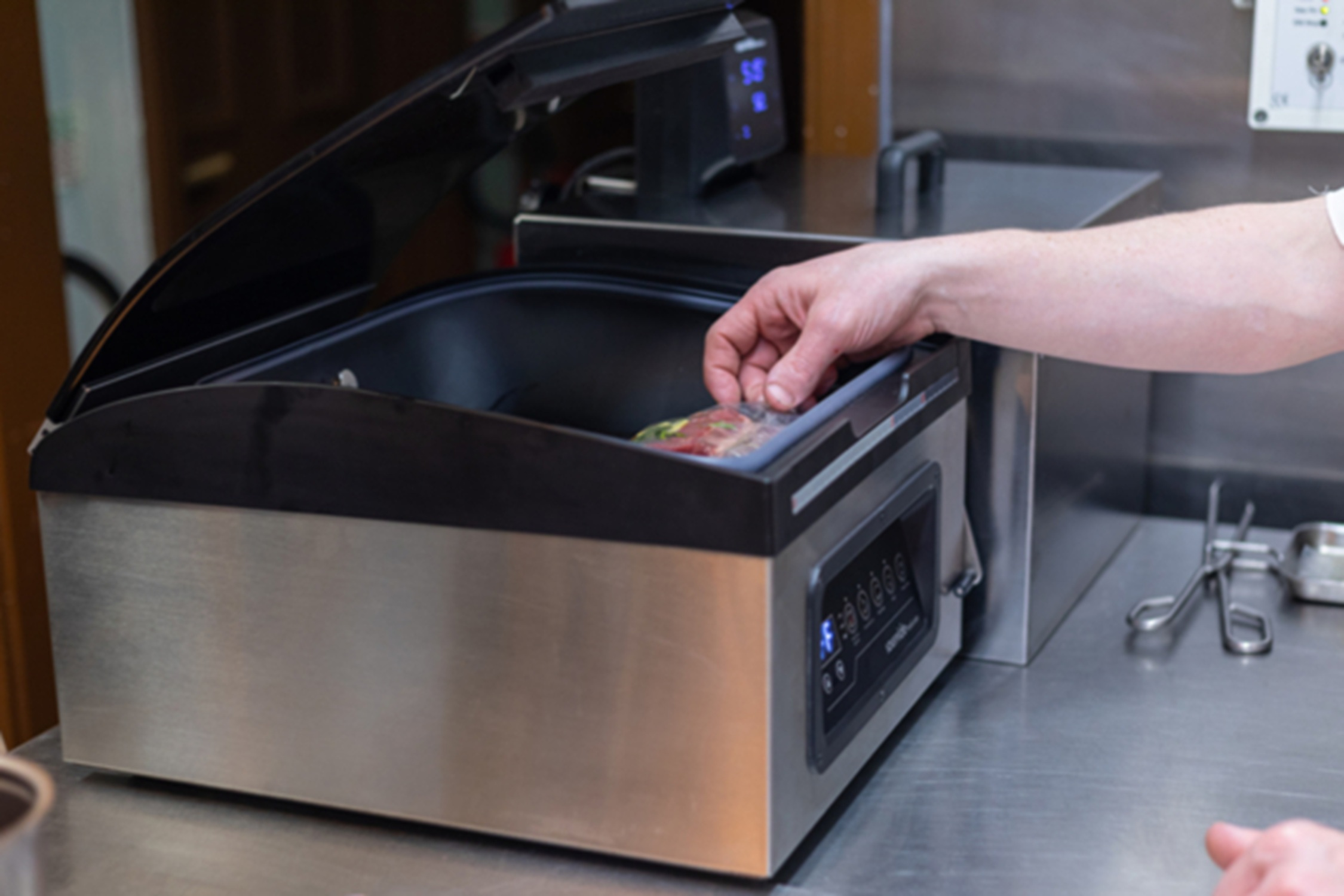 Een hand die eten in een vacuümsealer plaatst. RVS machine.