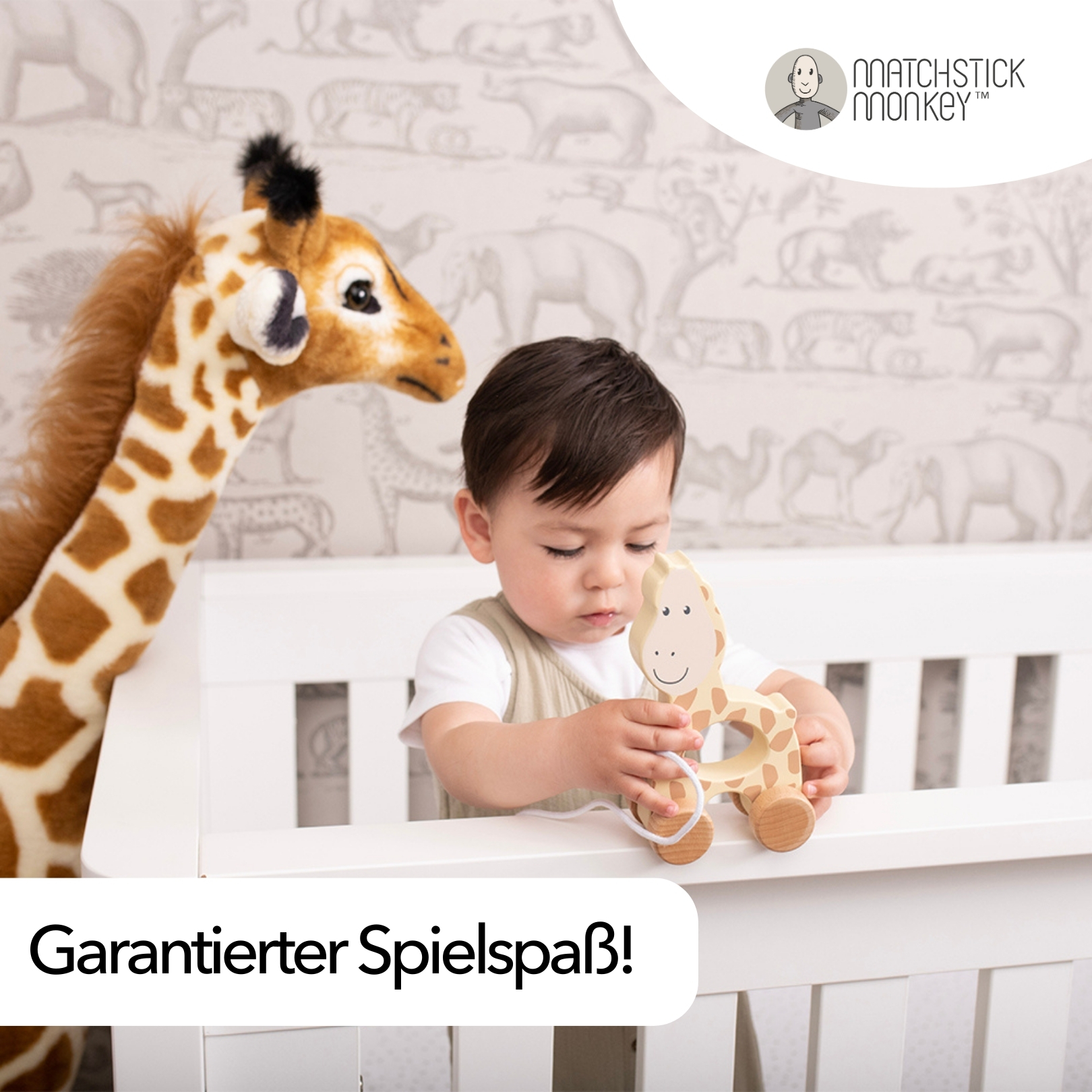Ein Baby spielt mit einem Holz-Giraffen-Spielzeug. Ein Giraffen-Spielzeug steht neben dem Baby in einem weißen Kinderbett.