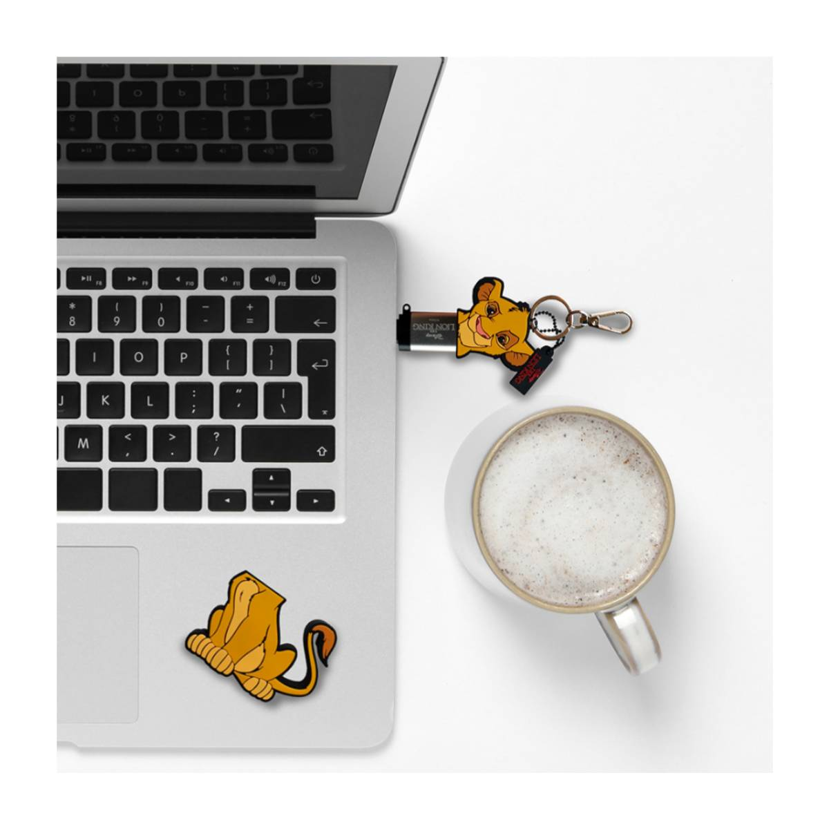 Laptop mit USB-Stick und einer Tasse. Artikel zum Thema König der Löwen auf weißer Oberfläche.
