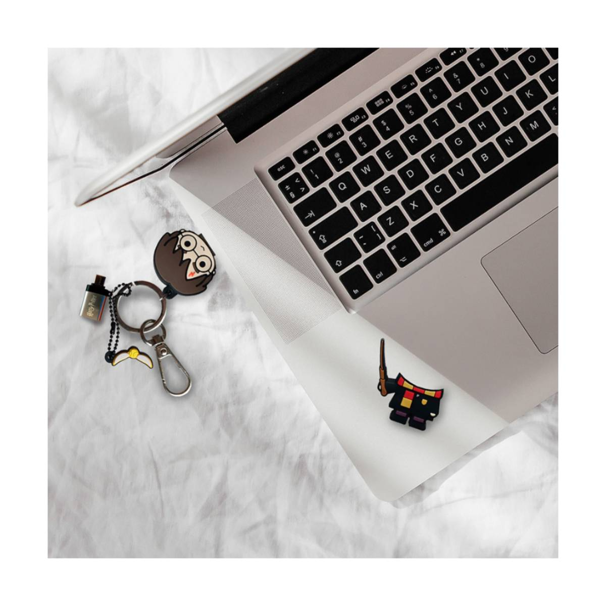 Ein Laptop, ein Schlüsselanhänger mit Harry Potter Figur und ein Anstecker liegen auf einem weißen Laken.