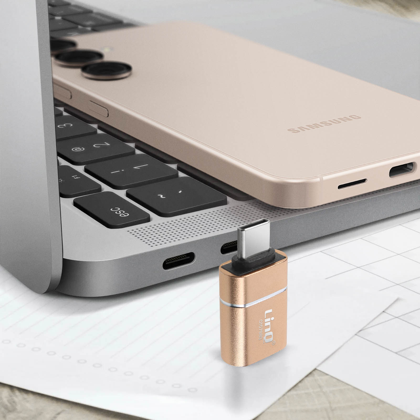 Un adattatore USB-C dorato accanto a un laptop e un telefono. Il telefono è beige.