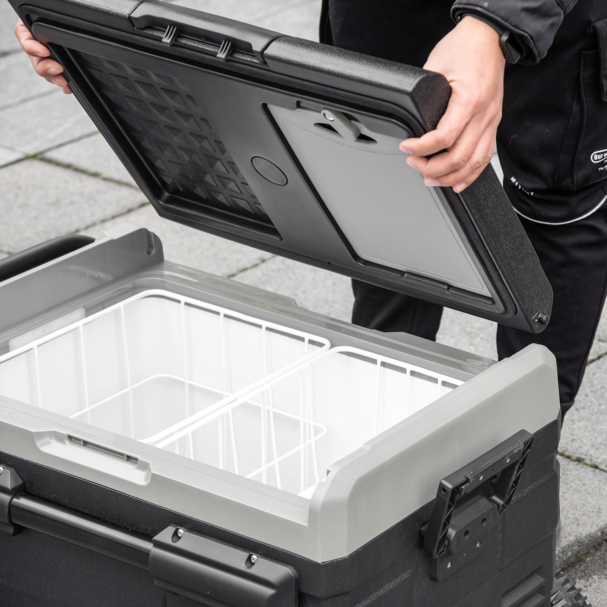Eine Person öffnet eine grau-schwarze Kühlbox. Die Kühlbox ist geöffnet und zeigt weiße Trennwände im Inneren.