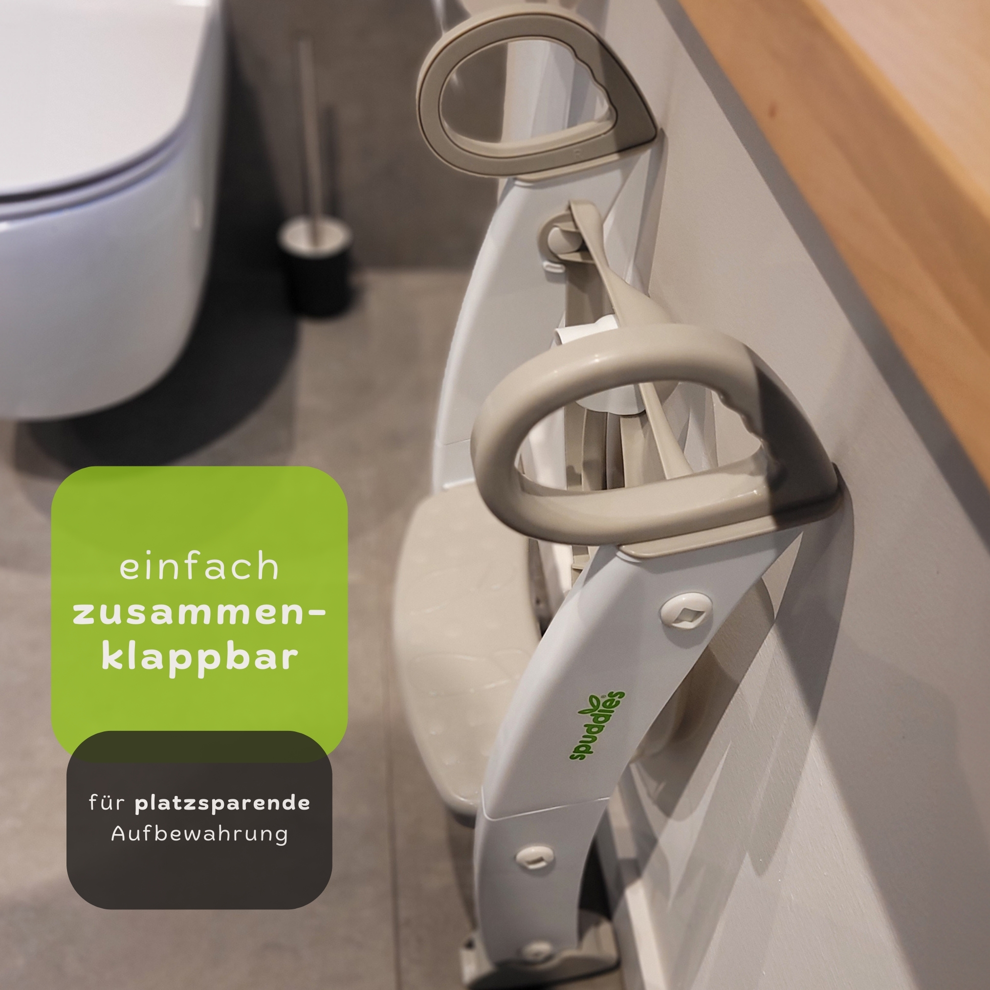 Klappbare Toilettenhilfe an einer Wand befestigt. Text: 'einfach zusammenklappbar'. Hintergrund: Toilette und Wand.