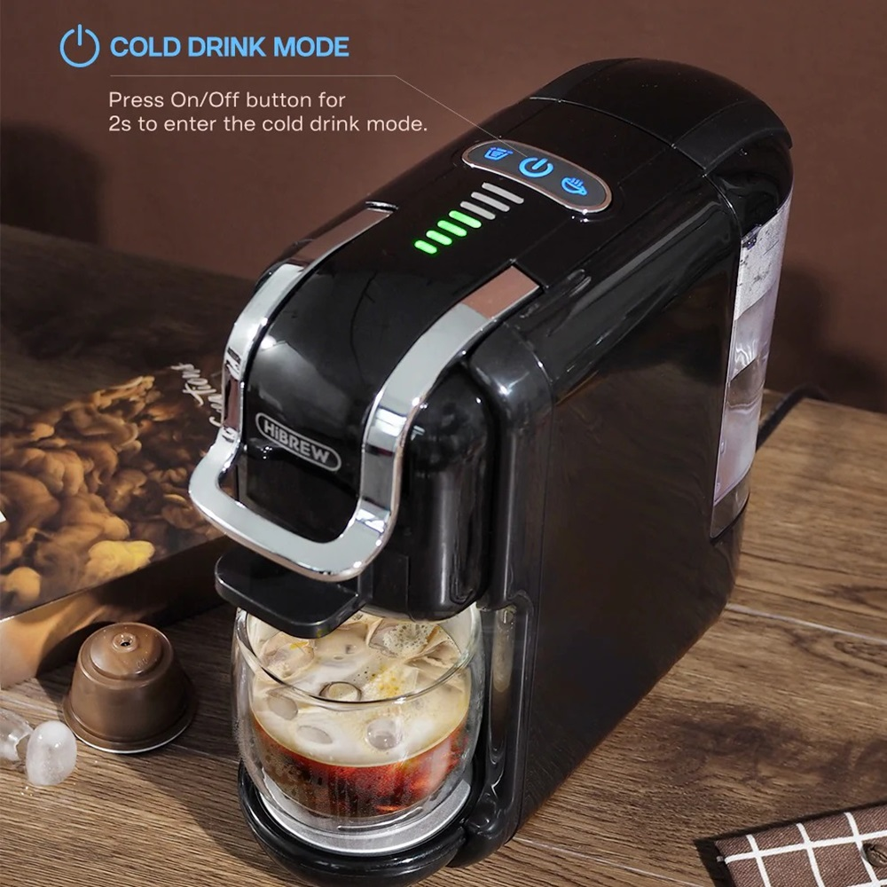 Schwarze Kaffeemaschine mit einem Glas, Eis und Kaffee darin. Dunkler Holztisch.