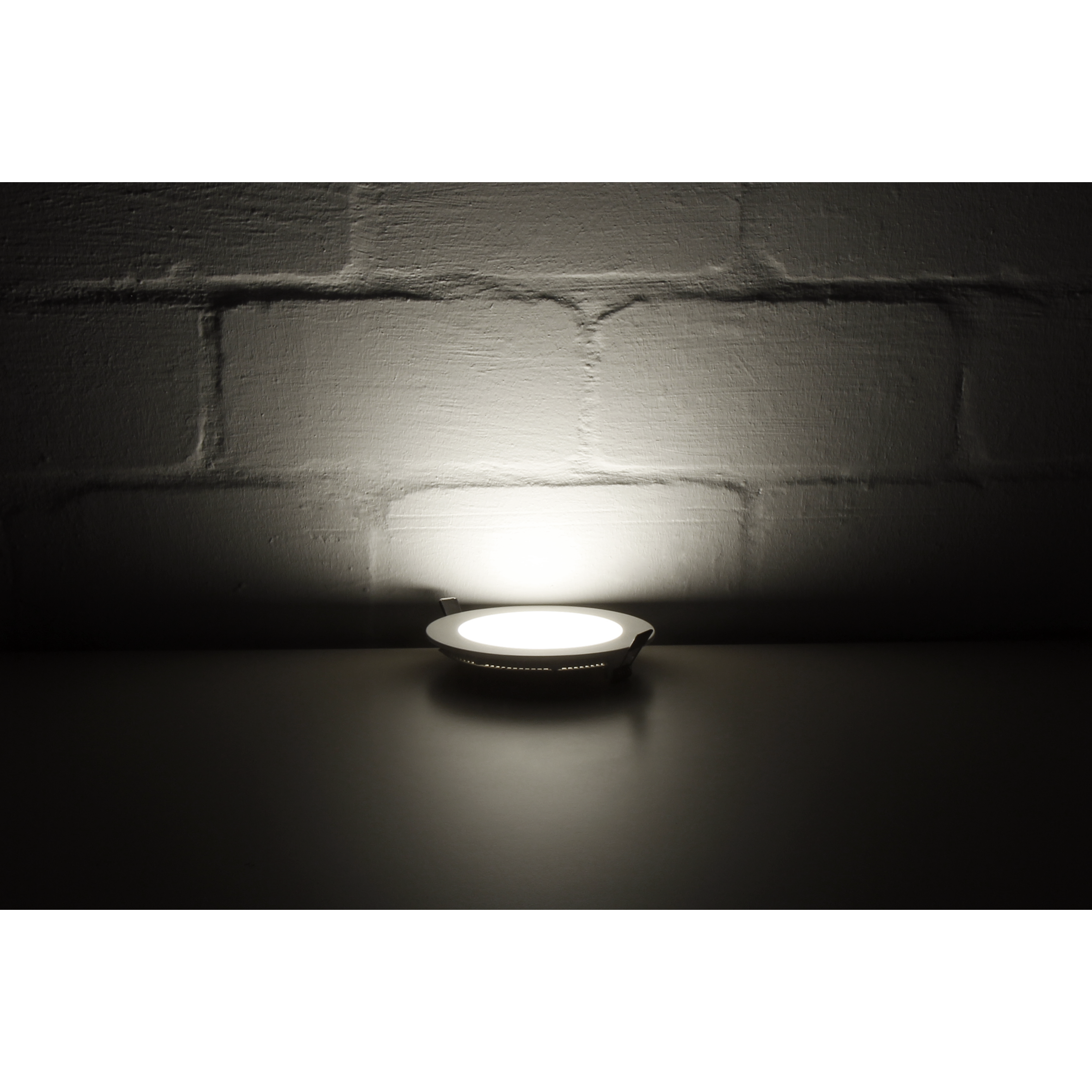 Ein kleines rundes Licht auf einer dunklen Oberfläche mit einer beleuchteten Wand dahinter.