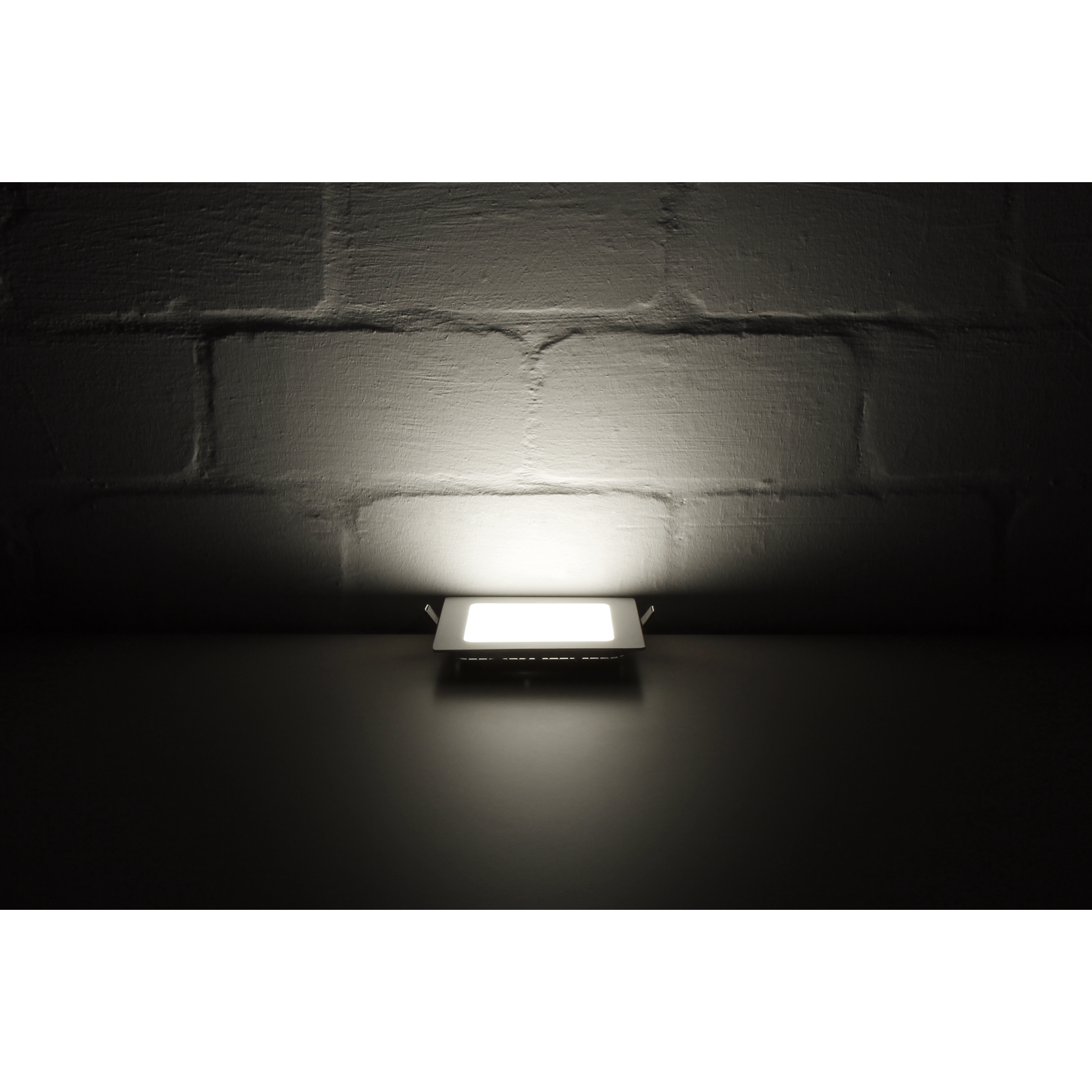 Ein quadratischer LED-Einbaustrahler auf dunklem Hintergrund. Er ist beleuchtet und an einer Ziegelmauer befestigt.