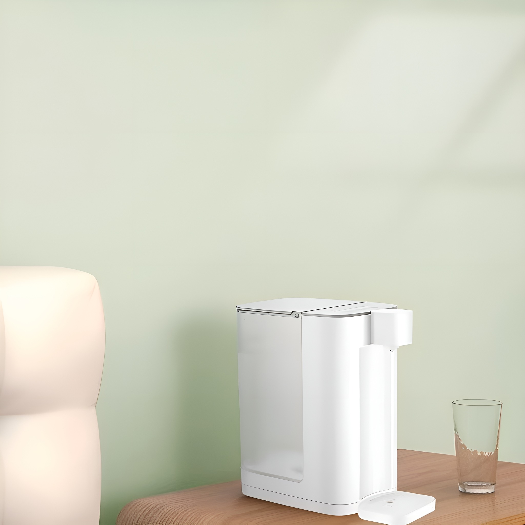 Weißer Wasserspender auf Holztisch mit Glas und kleiner weißer Fernbedienung. Grüne Wand.