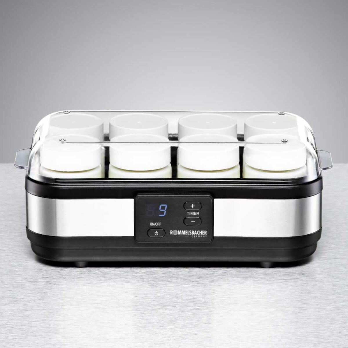 Ein Joghurtbereiter mit 8 weißen Gläsern und einem transparenten Deckel. Der Hintergrund ist grau.