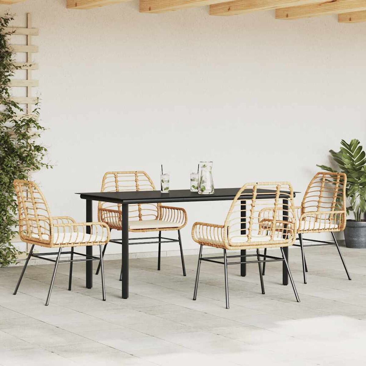 Set da pranzo all'aperto con tavolo nero, sedie in rattan e bevande. Sfondo con parete bianca.