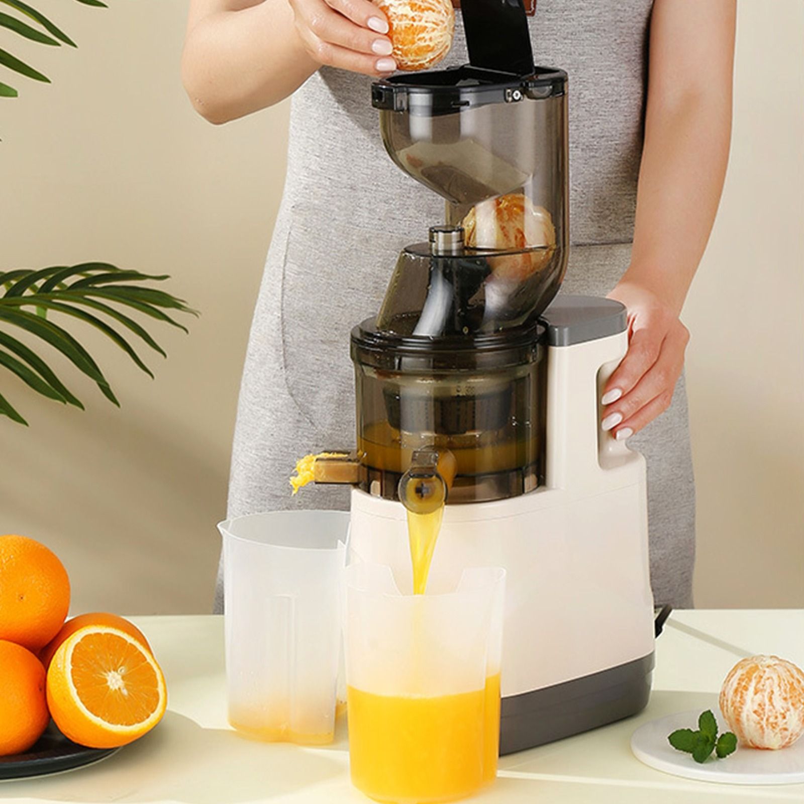 Frau beim Auspressen von Orangen. Eine Orange wird hinzugefügt. Entsafter und Krug werden verwendet. Der Saft fließt.