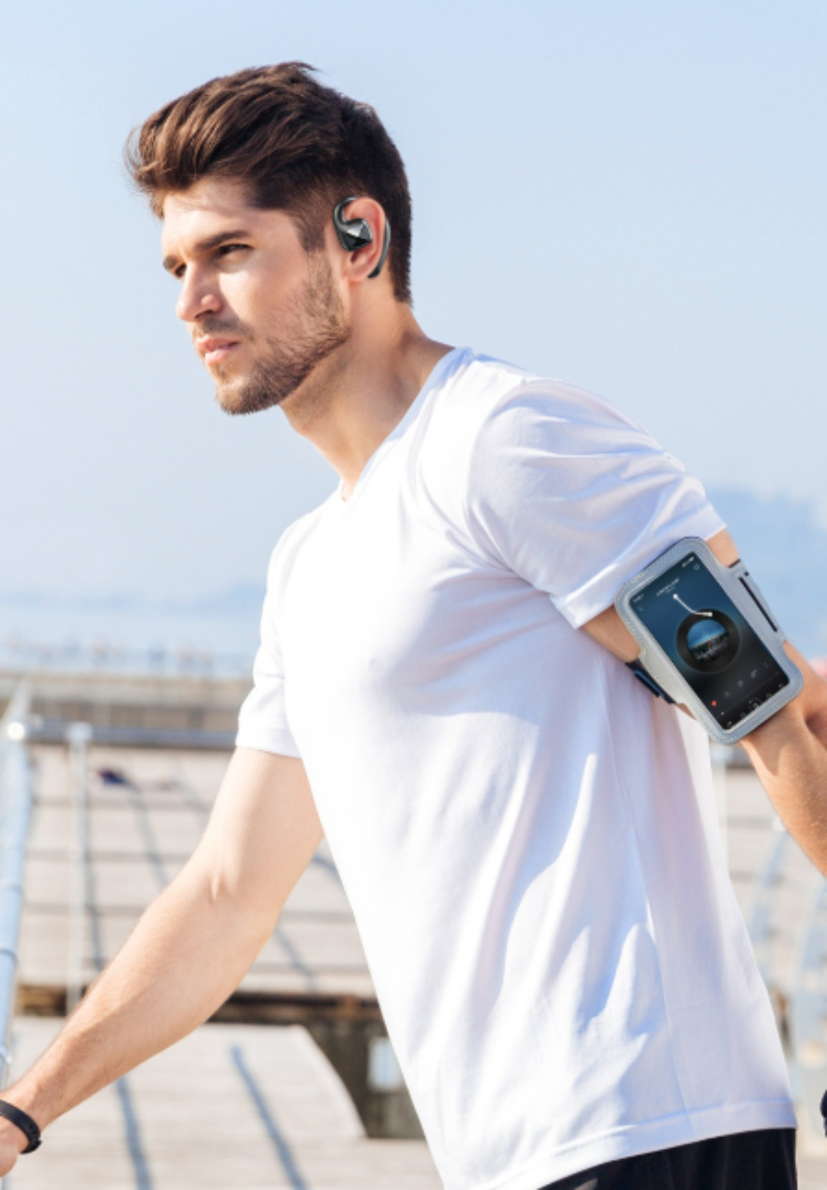 Mann mit Ohrhörer, weißem Hemd, Armband mit Telefon. Blauer Himmel im Hintergrund.