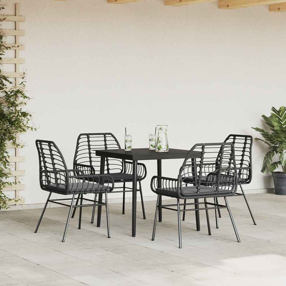 Set da patio esterno con tavolo e sedie nere. Quattro sedie attorno a un tavolo, con piante e un muro bianco.