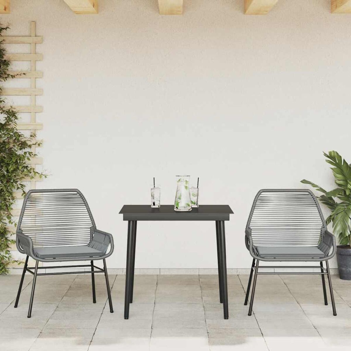 Zwei graue Stühle und ein schwarzer Tisch auf einer Terrasse. Grünpflanzen links und rechts.