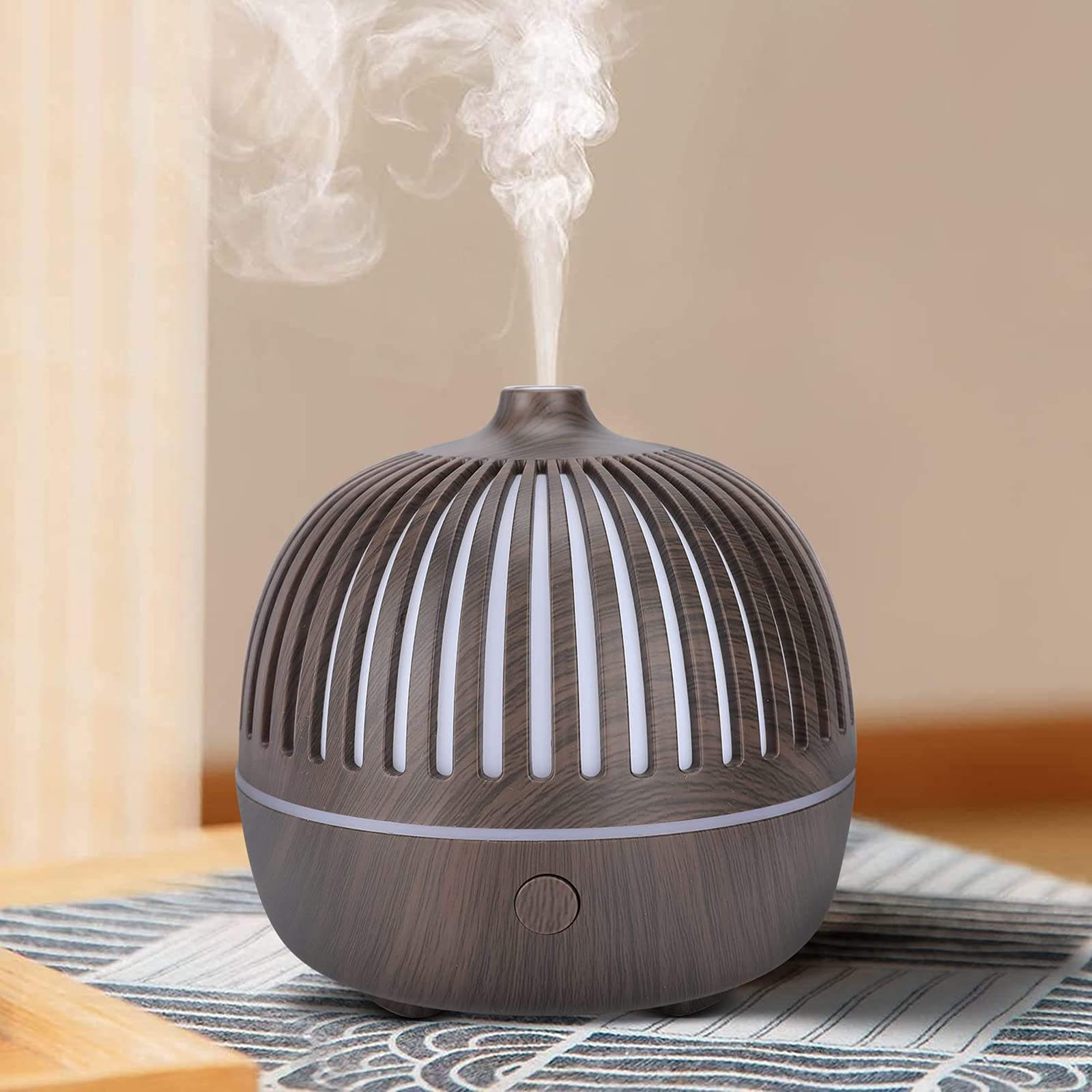 Ein holzmaserter Aromadiffusor mit aufsteigendem Dampf. Er steht auf einem gemusterten Tuch.