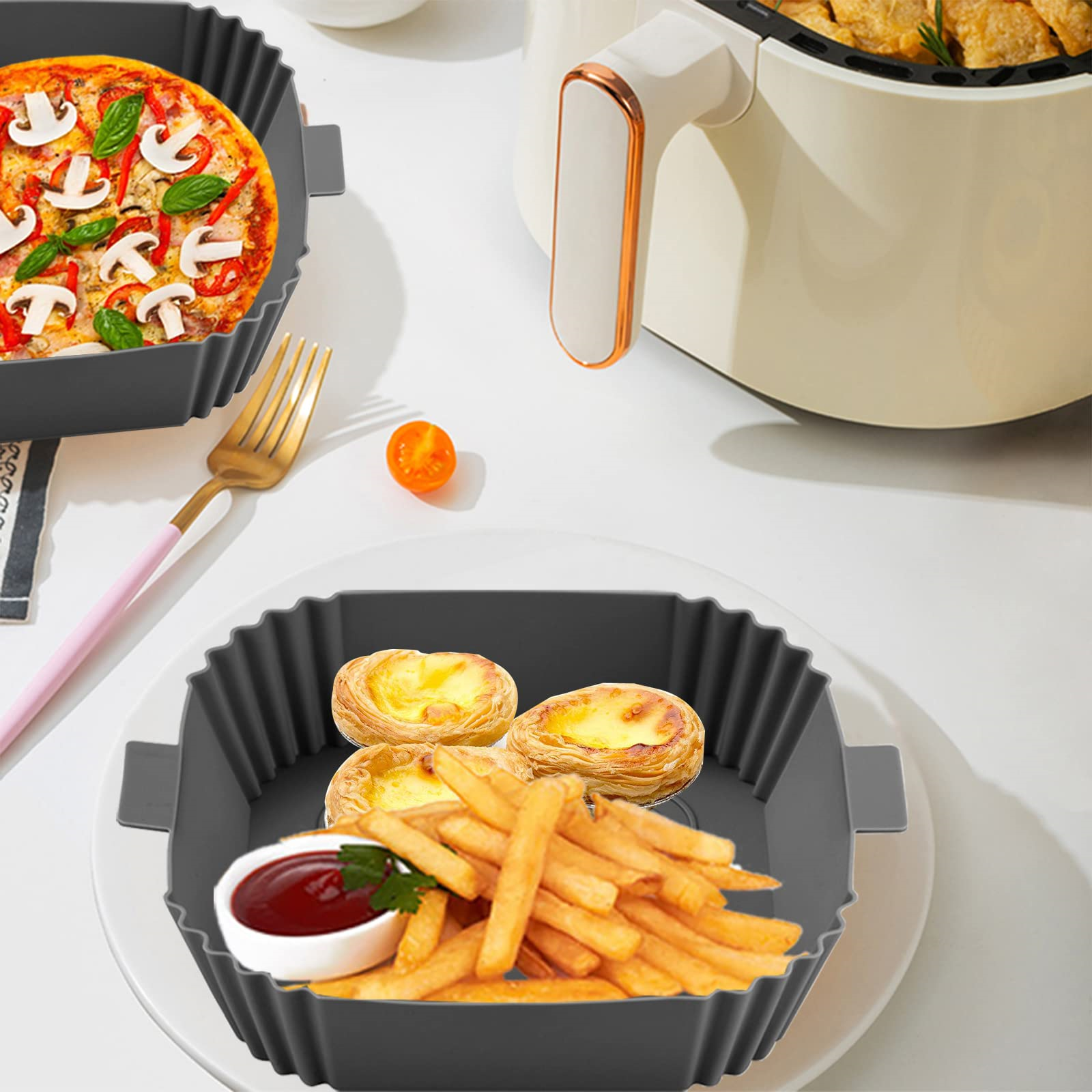 Eine Heißluftfritteuse mit Pizza, Pommes und Gebäck in Schalen auf weißer Oberfläche.