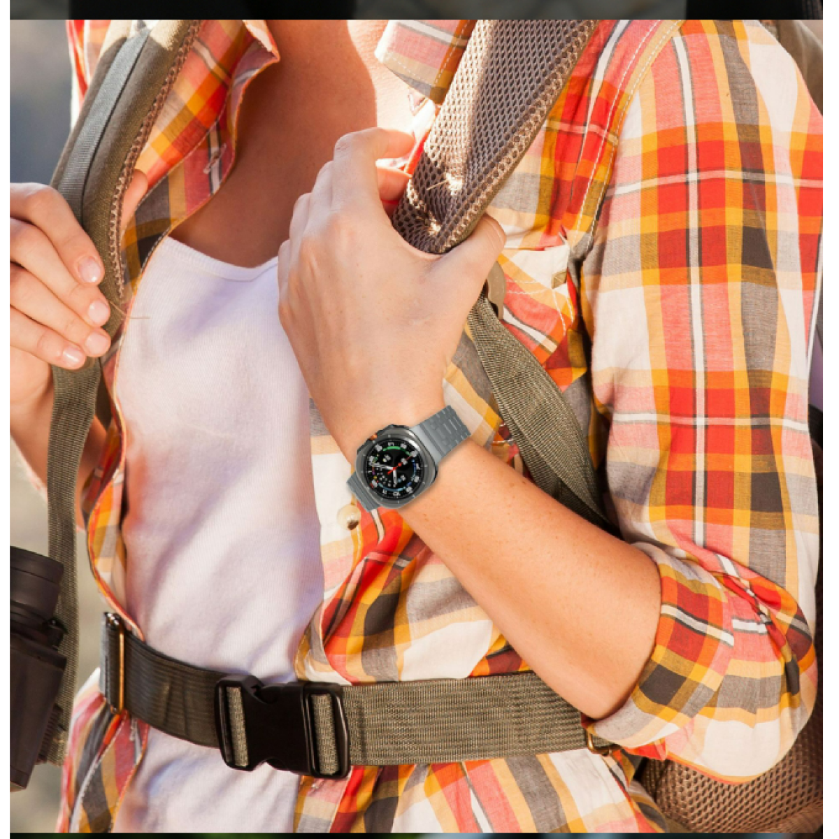 Una persona che indossa uno smartwatch grigio con quadrante nero. Indossa una camicia a quadri ed è all'aperto.