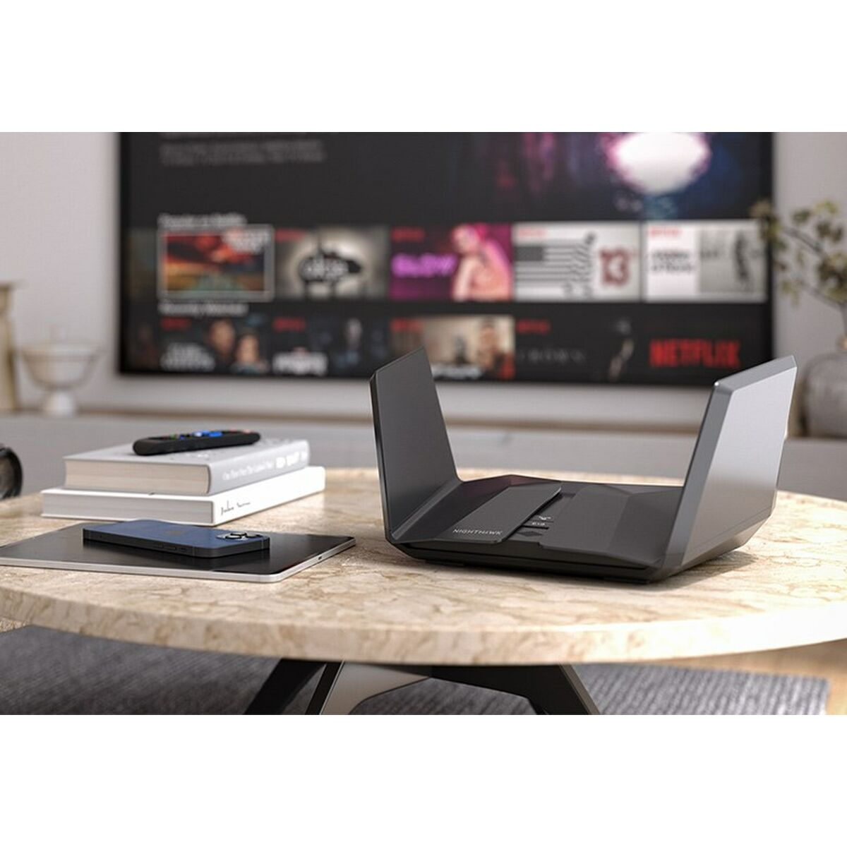 Czarny router stoi na stole ze smartfonem, książkami i pilotem. W tle widoczny jest telewizor.