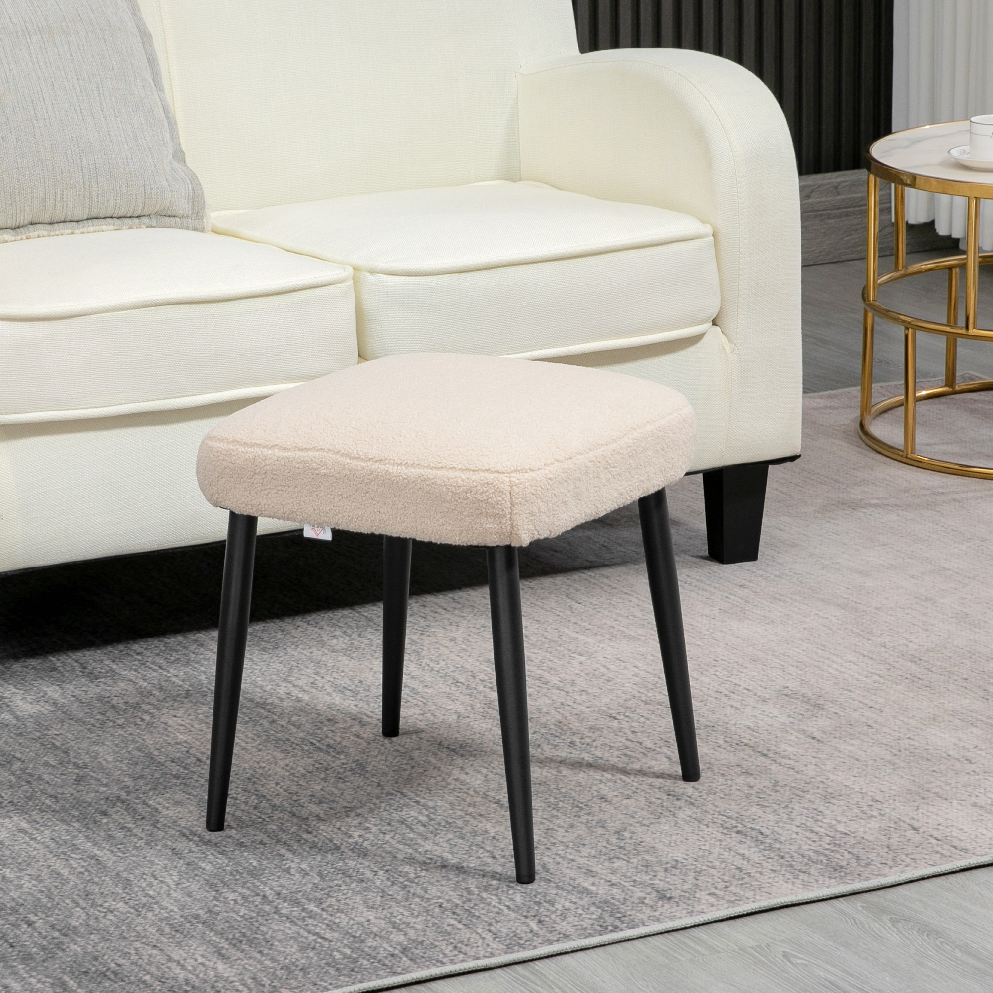 Beiger gepolsterter Hocker mit schwarzen Beinen, auf einem Teppich neben Sofa.