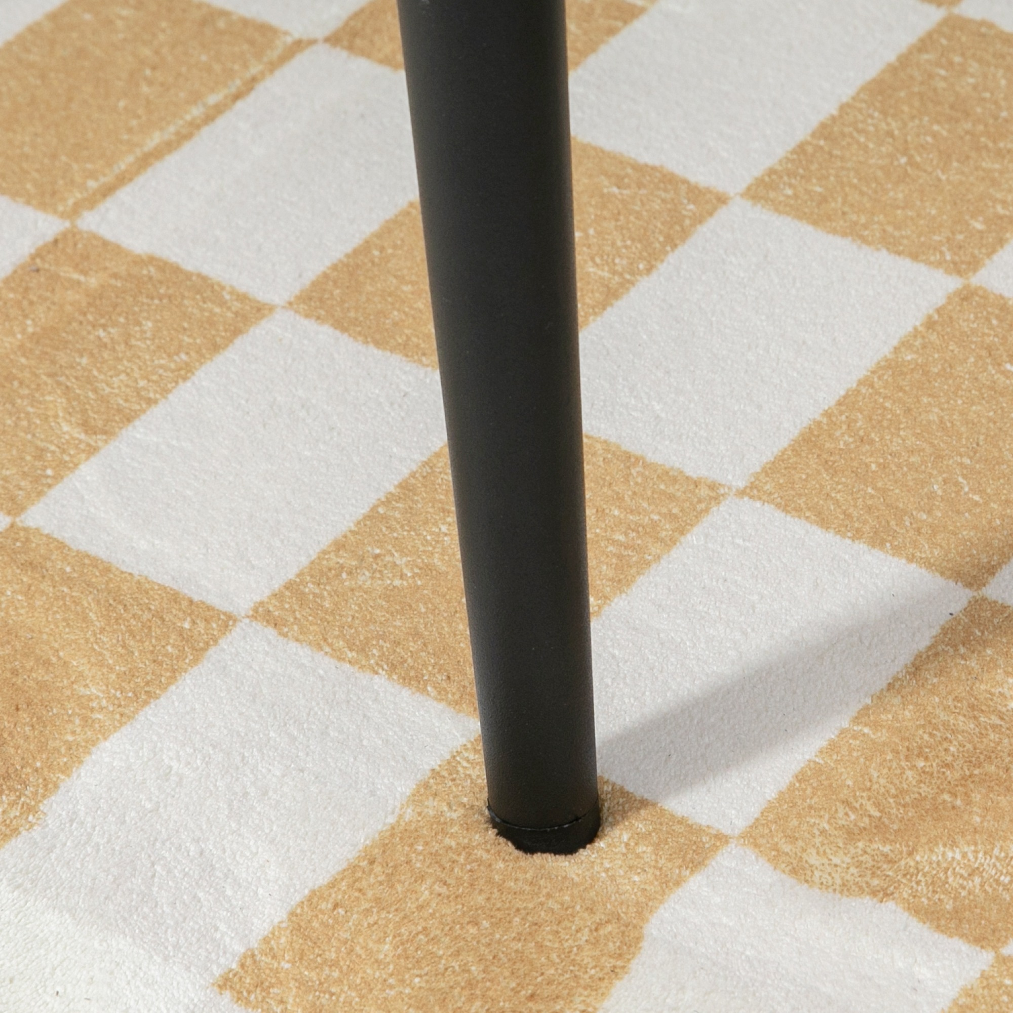 Nahaufnahme eines schwarzen Stuhlbeins auf einem karierten beige-weißen Teppich.