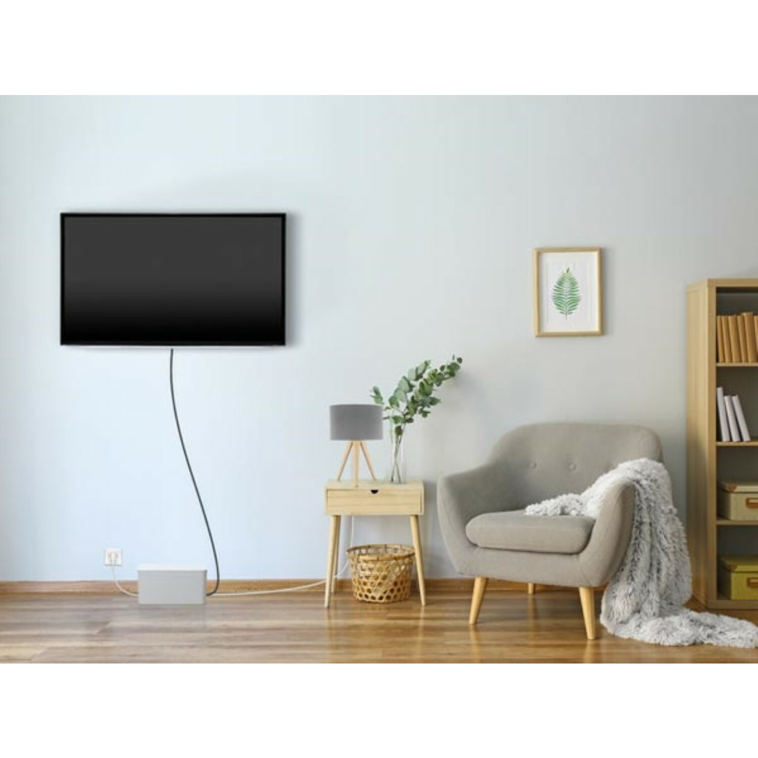 Telewizor na ścianie, stolik nocny z lampą i szary fotel z kocem.