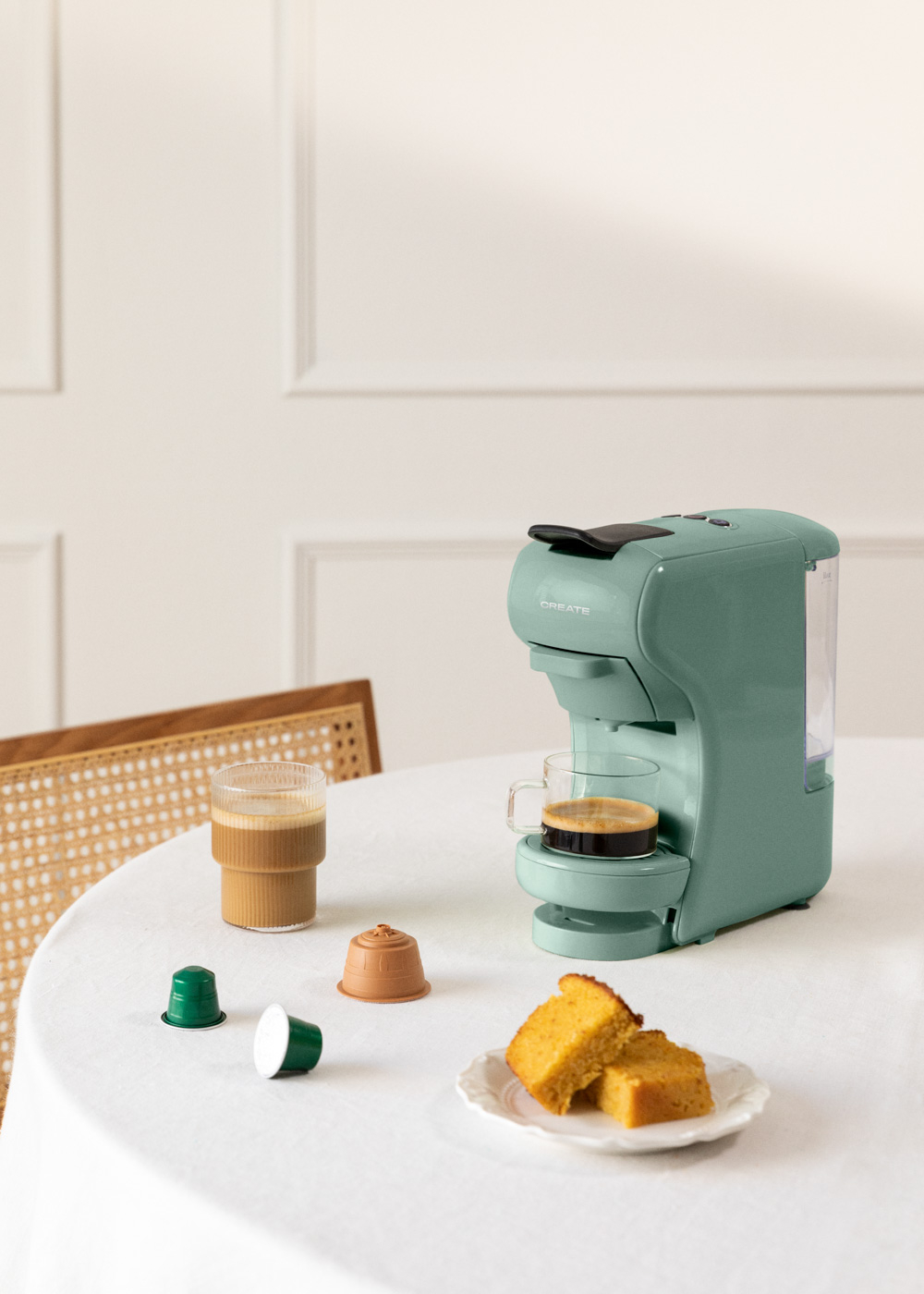 Cafetera verde menta, café, dos cápsulas de café y pastel en una mesa blanca.