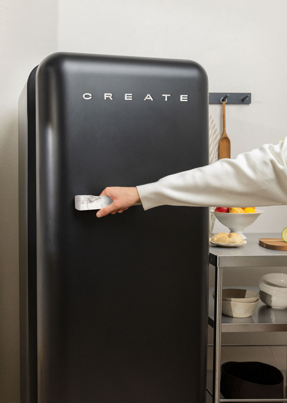 Una persona abre un refrigerador negro retro en un entorno de cocina. Se ve un carro de acero inoxidable.