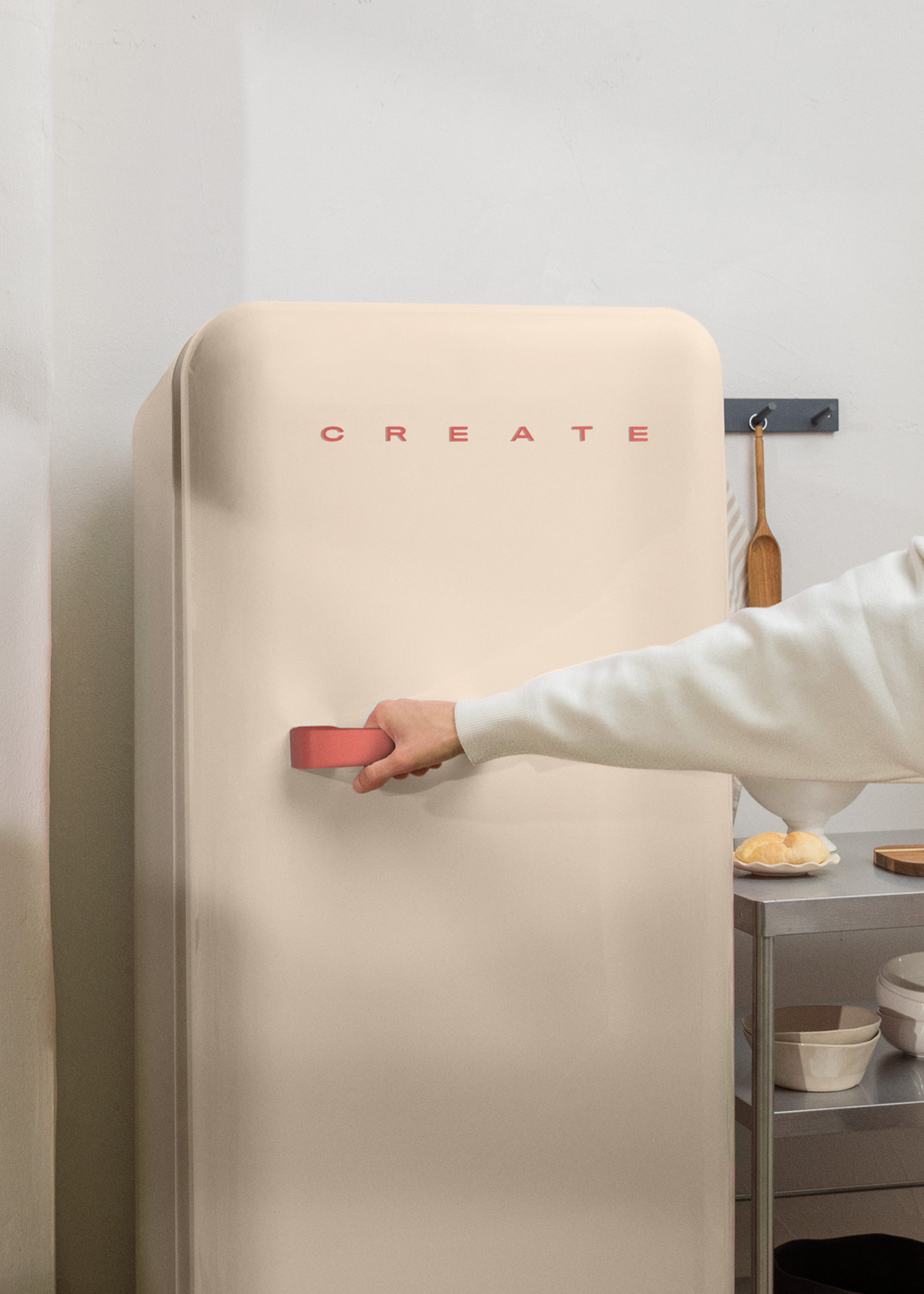 La mano de una persona abriendo un refrigerador beige con letras rojas que deletrean CREATE en el frente.