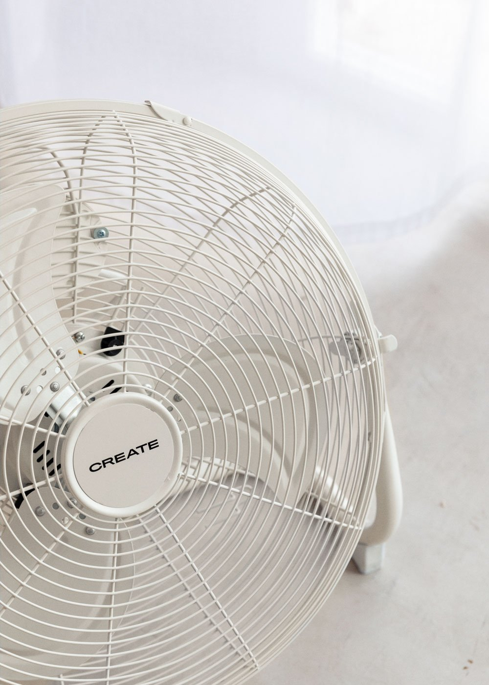 Un ventilador CREATE blanco con un diseño circular. Tiene un asa y está sobre un suelo claro.