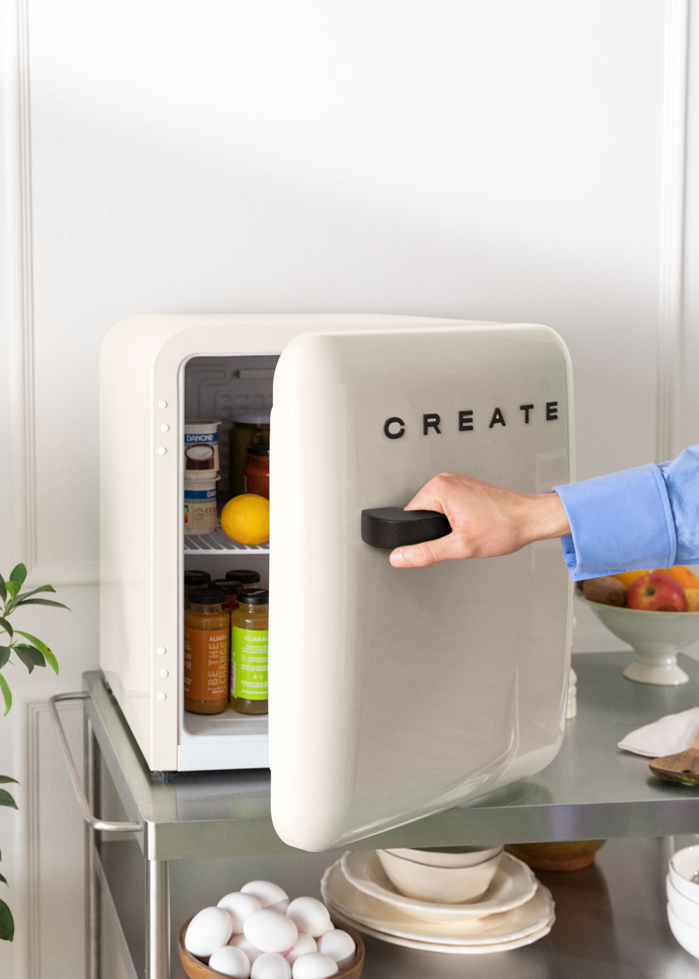 Un mini-frigorífico color crema con "CREATE" en la puerta, que se abre con una mano.