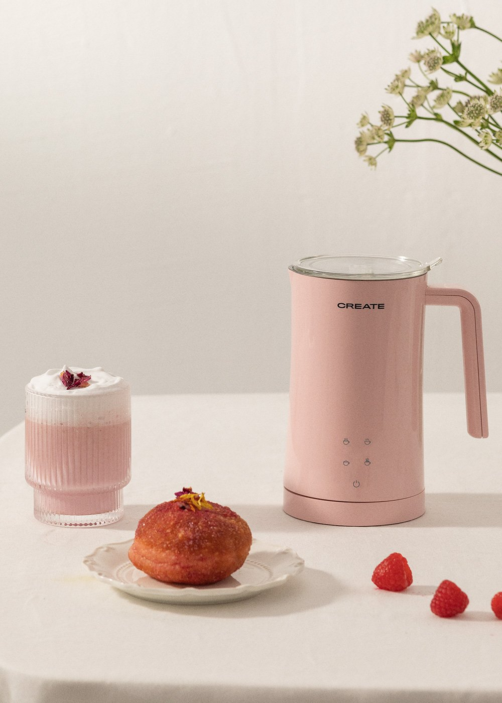 Un espumador de leche Create rosa con un vaso de bebida rosa y un donut.