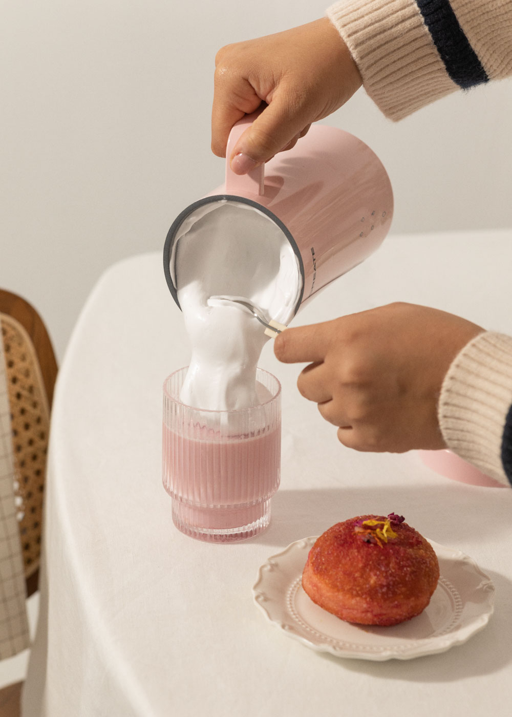 Persona vertiendo espuma rosa en vaso, con pastel rosa en plato.