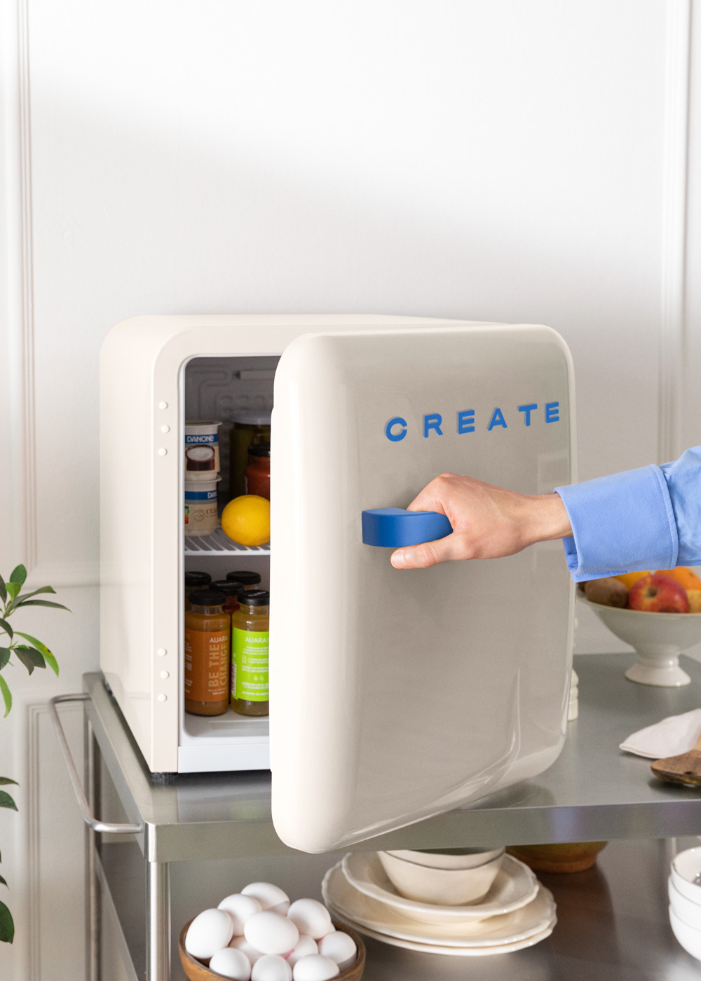 Nevera crema con CREATE azul. Mano abre la puerta mostrando comida. Carrito con fruta y cuencos.