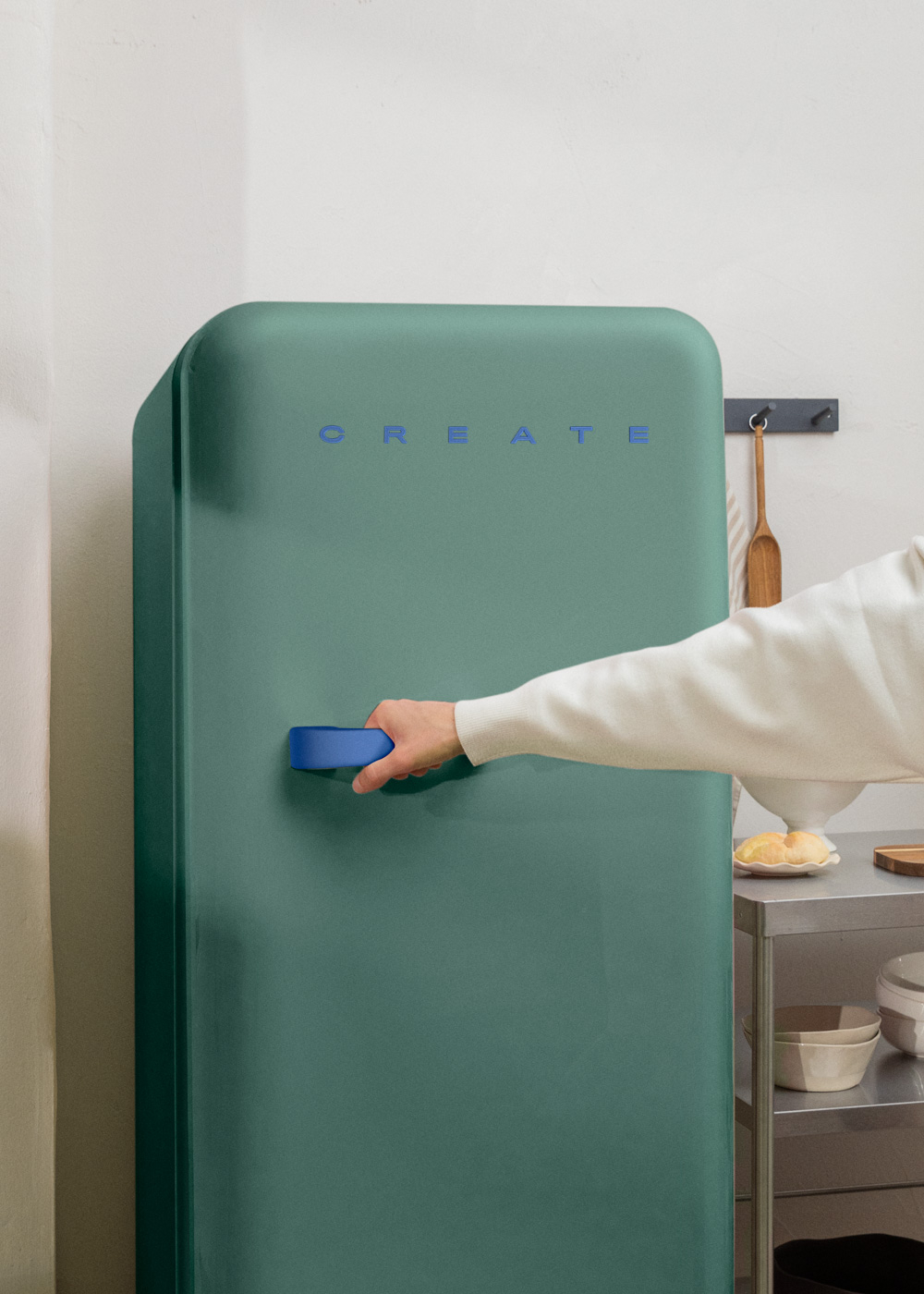 Un refrigerador color turquesa, una persona abriendo la puerta. Fondo de cocina con comida y utensilios.