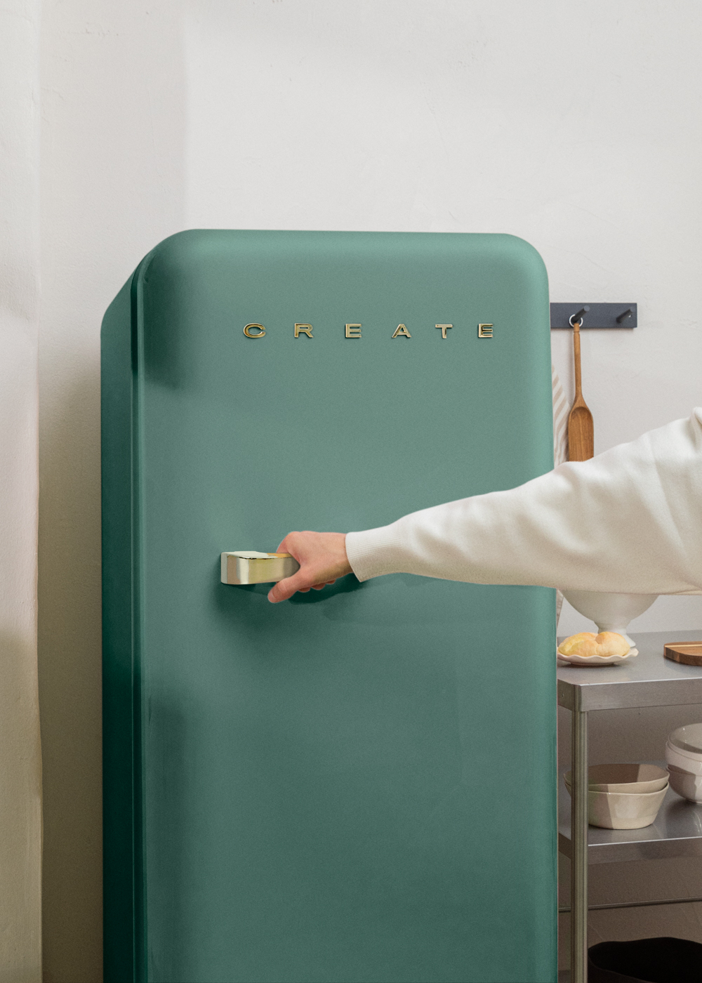Persona abriendo nevera verde. 'CREATE' en dorado. Cocina con estantes y objetos.