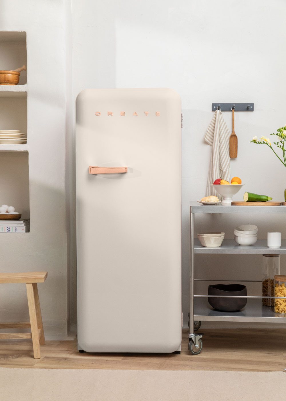 Nevera retro beige. Un taburete de madera y un carrito metálico con alimentos cerca.
