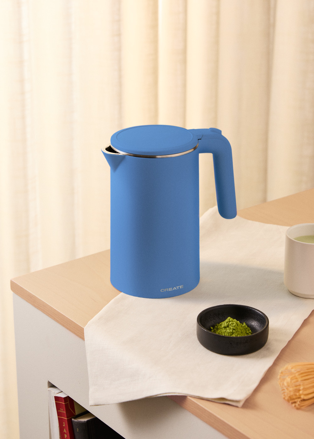 Hervidor eléctrico azul CREATE sobre mesa madera. Polvo matcha y taza presentes.