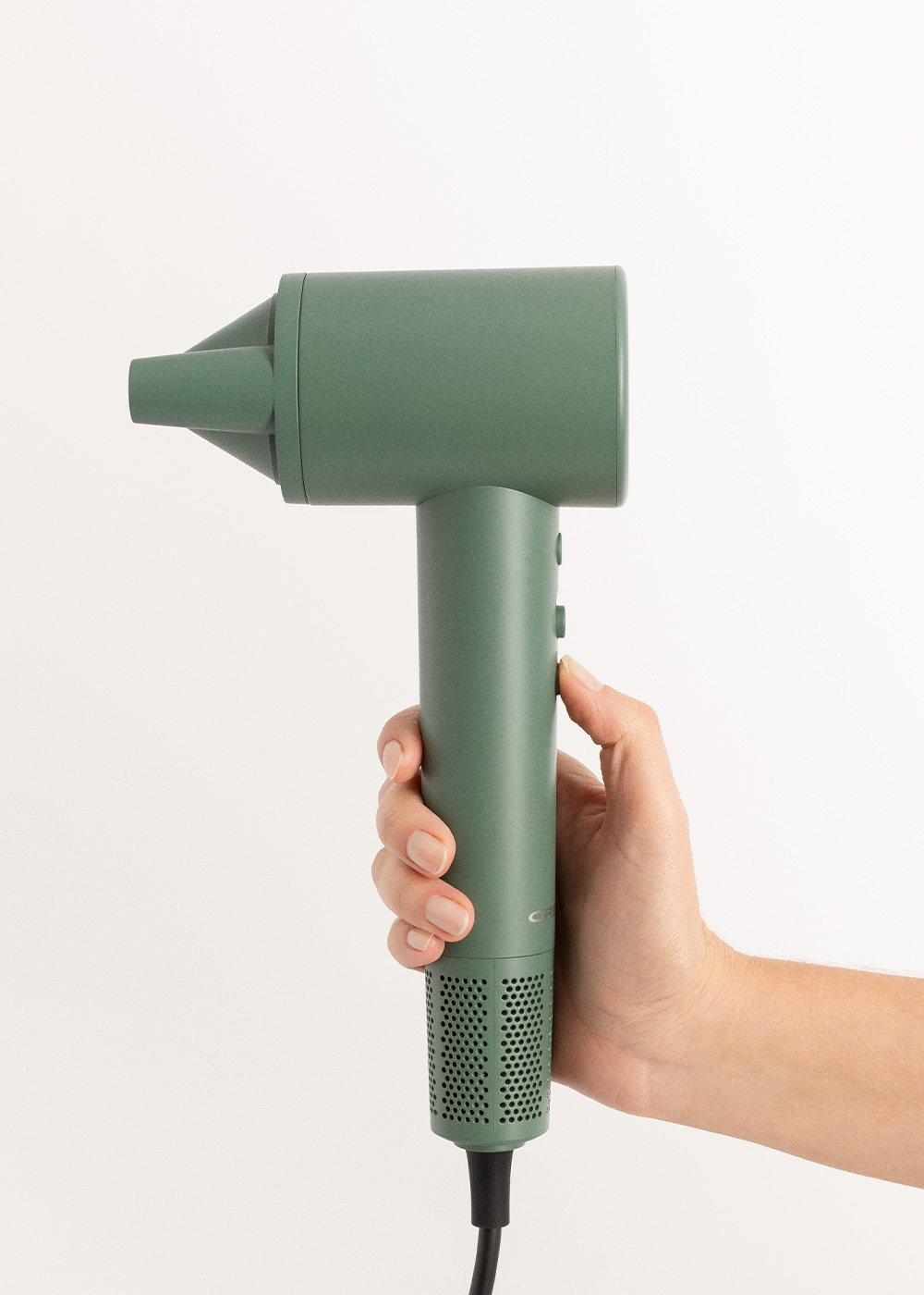 Una mano sostiene un secador de pelo verde. El secador está inclinado a la izquierda.