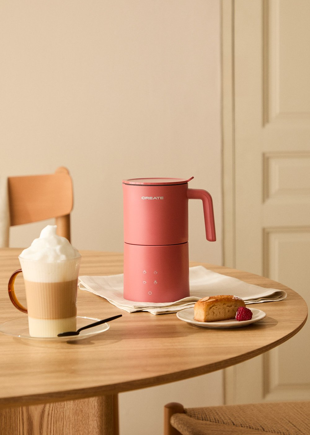 Cafetera rosa, una taza de latte, un pastel y una servilleta en una mesa de madera.