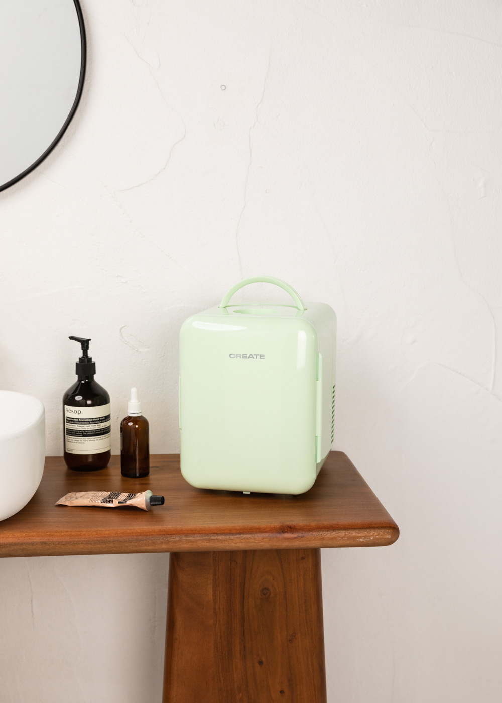 Mini-nevera verde con 'CREATE' en el frente, sobre una mesa de madera. Entorno de baño.