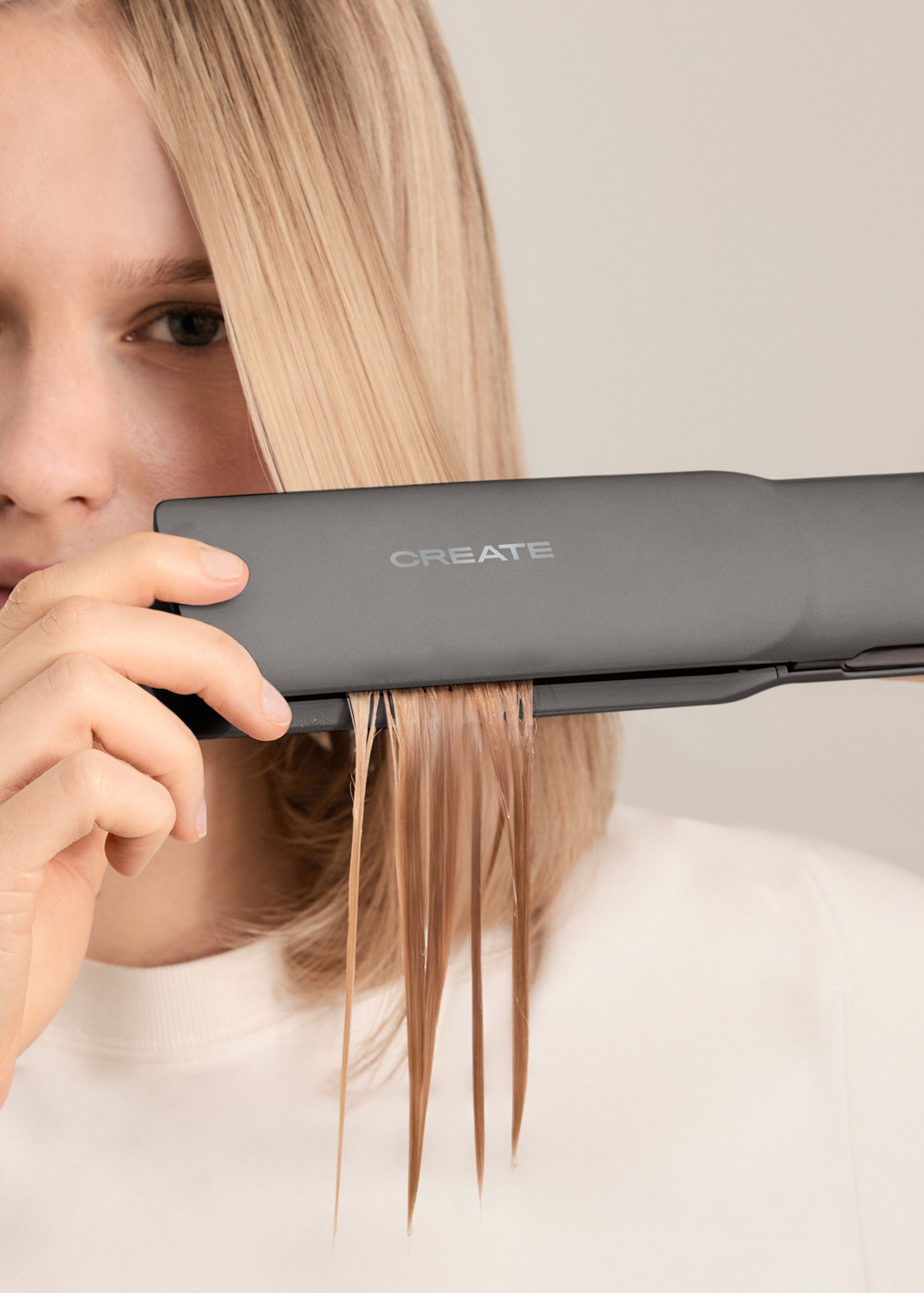 Una mujer usa una plancha de pelo en su cabello. La plancha tiene la palabra 'CREATE'.