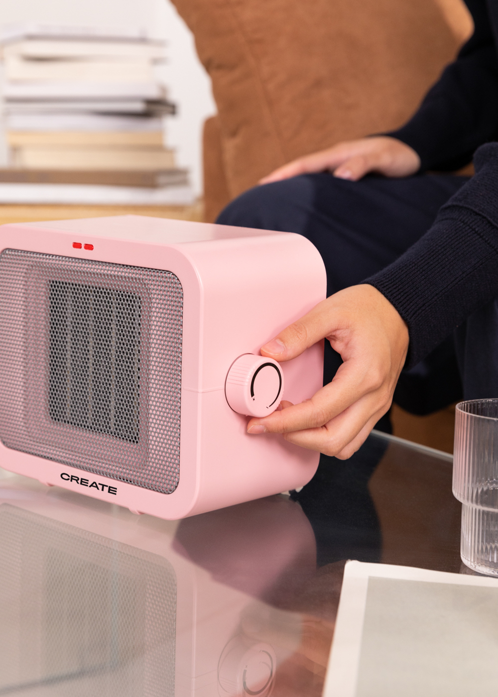 Un calefactor rosa con una persona ajustando el dial de temperatura. El calefactor está en una mesa de cristal.