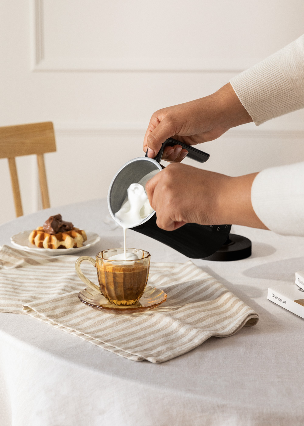 Una persona vierte espuma de leche en una taza de café sobre una mesa con un gofre y una servilleta.