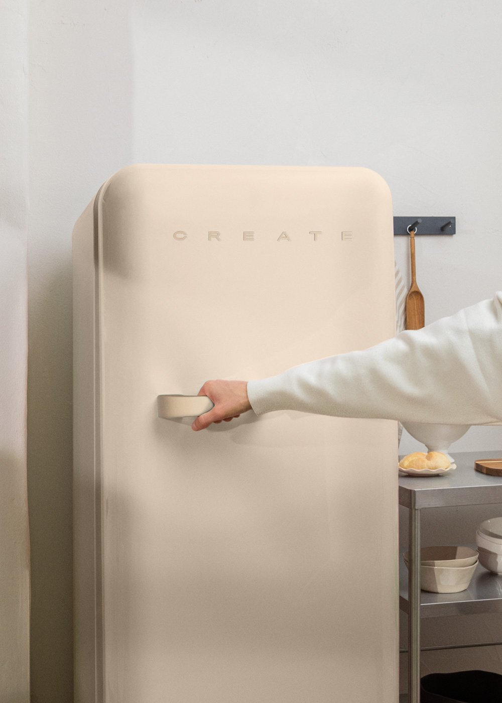 Refrigerador retro color crema. Una mano toca el asa. La palabra CREATE está impresa en la puerta.