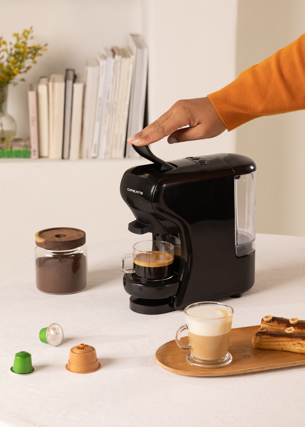 Una cafetera negra operada por una mano. Café, tazas y pasteles alrededor.