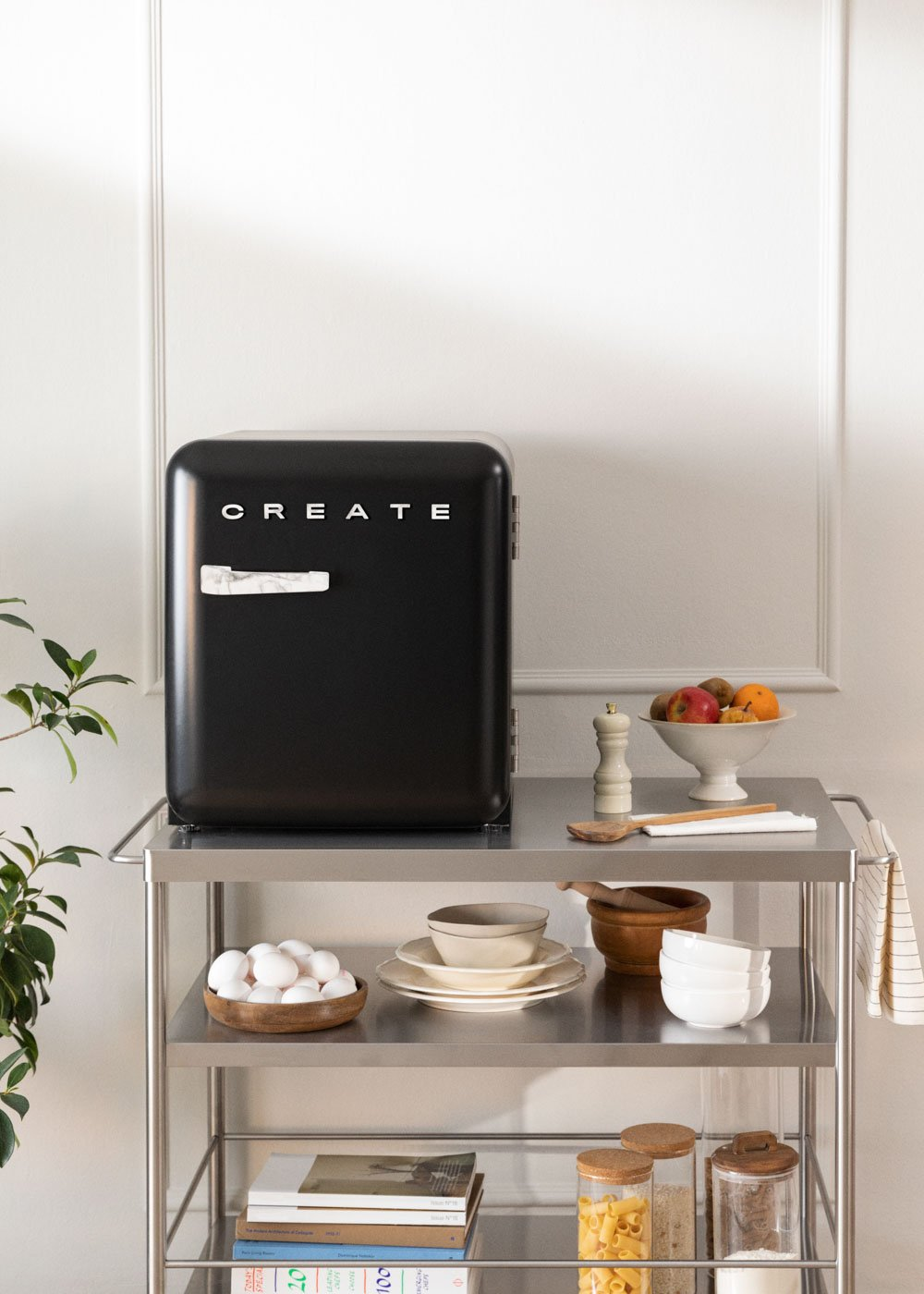 Un refrigerador negro con la palabra CREATE está en un carrito de acero inoxidable con alimentos y platos.