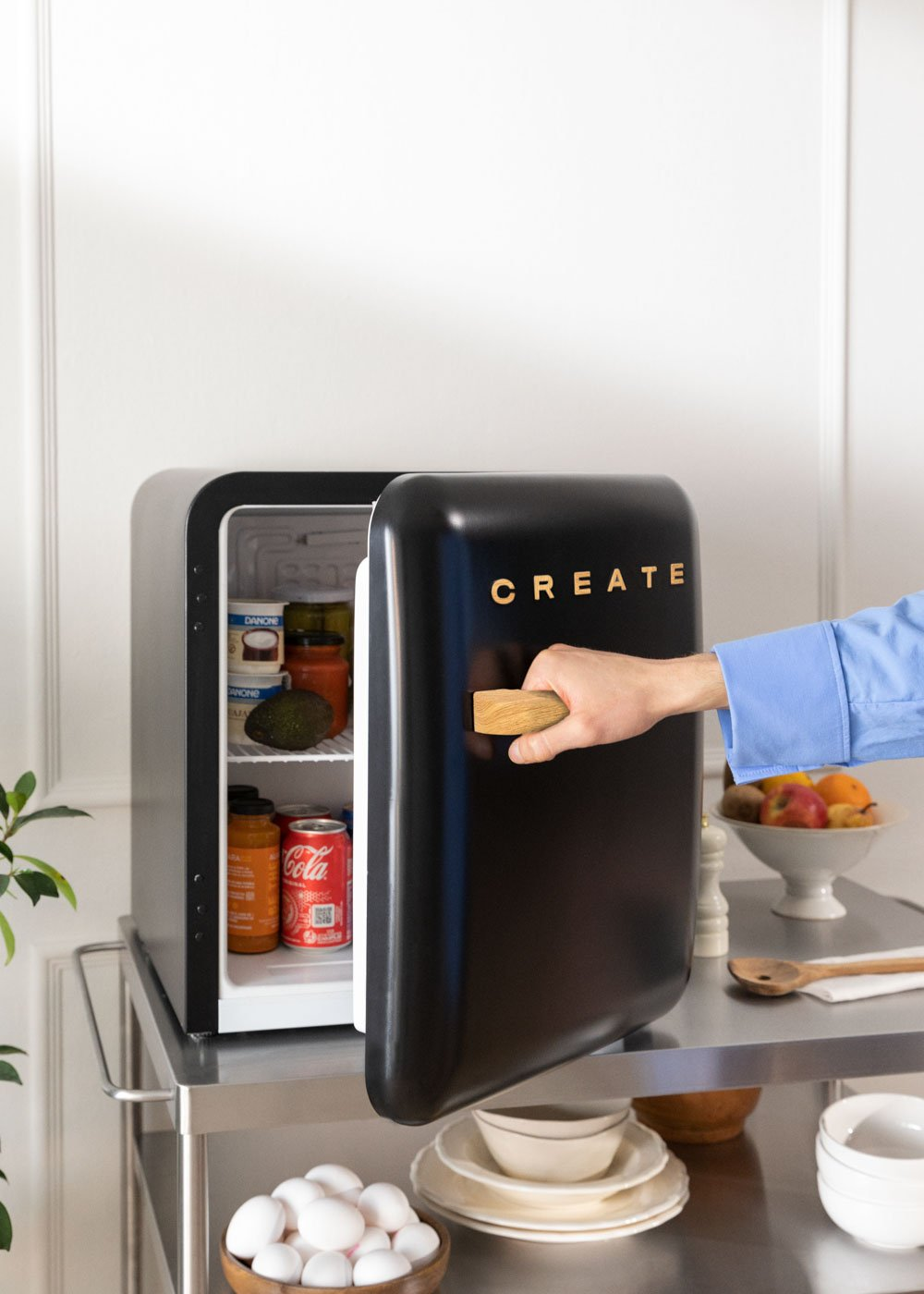 Refrigerador negro con puerta abierta. Mano abriéndola. Dentro: comida y bebidas. 'CREATE' en dorado.
