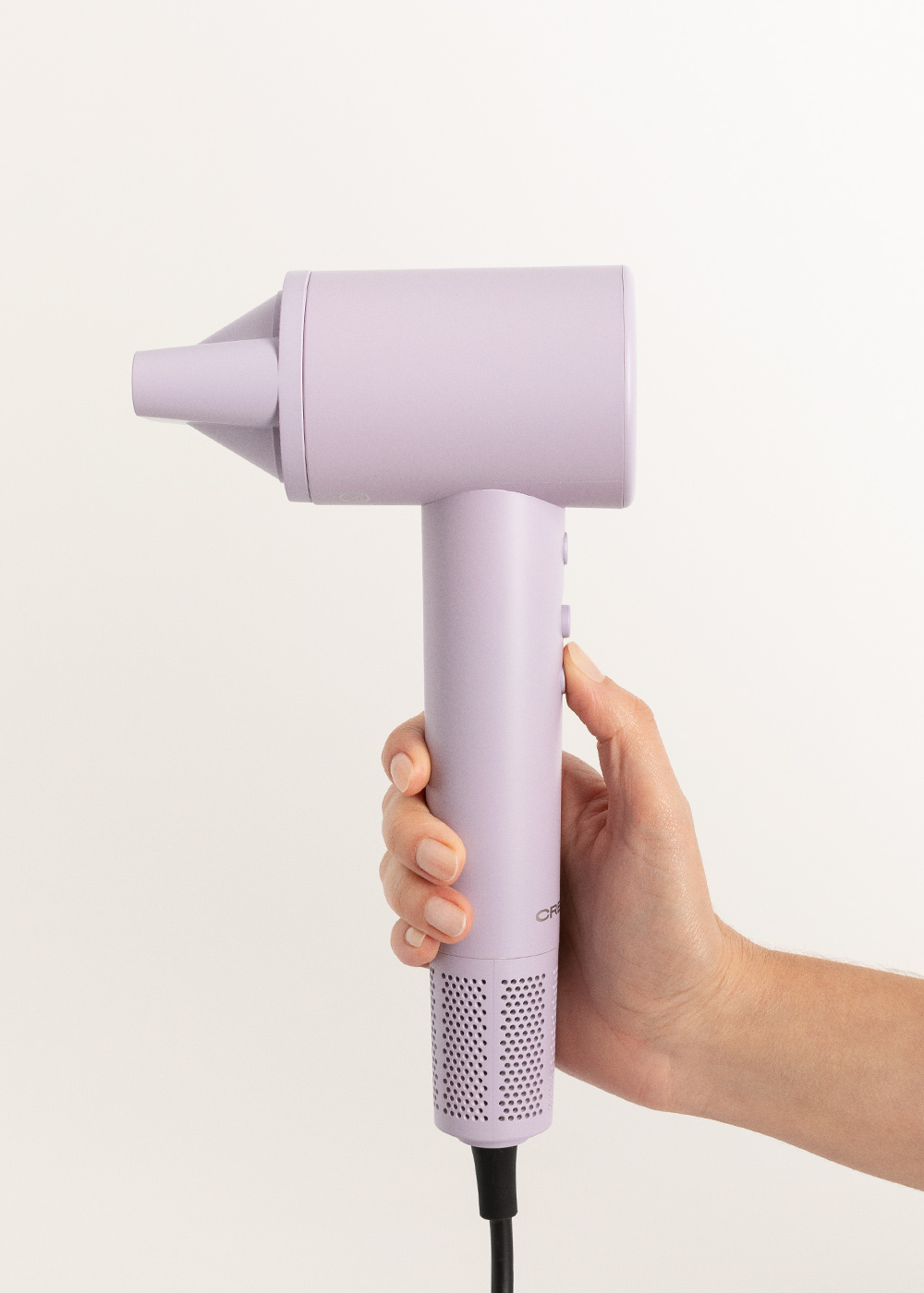 La mano de una persona sostiene un secador de pelo morado. El fondo es blanco.