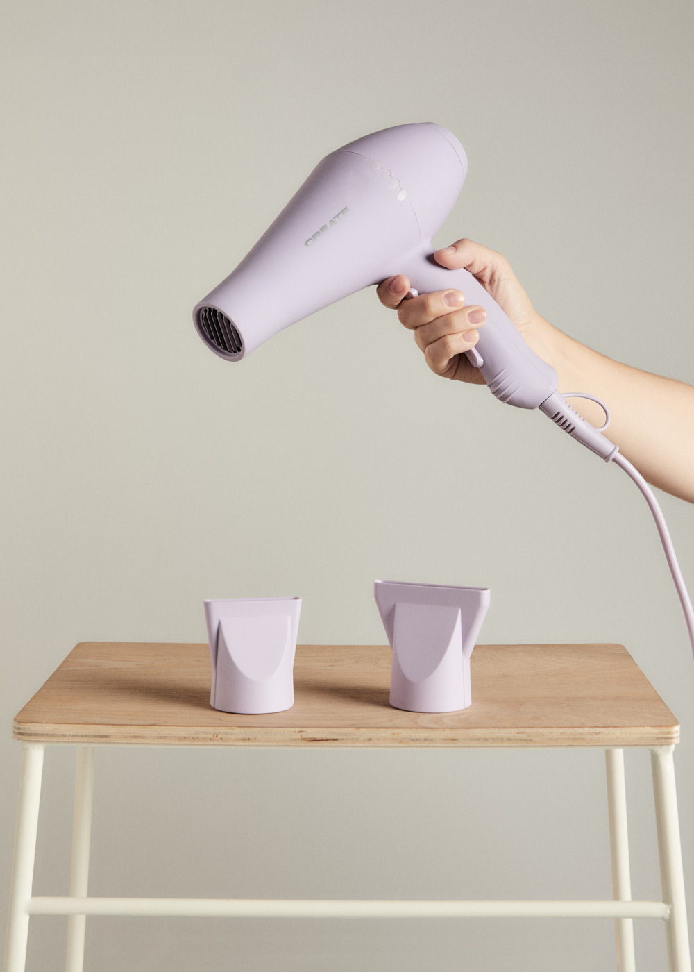 Una persona sostiene un secador de pelo morado claro. Dos accesorios sobre una mesa de madera.