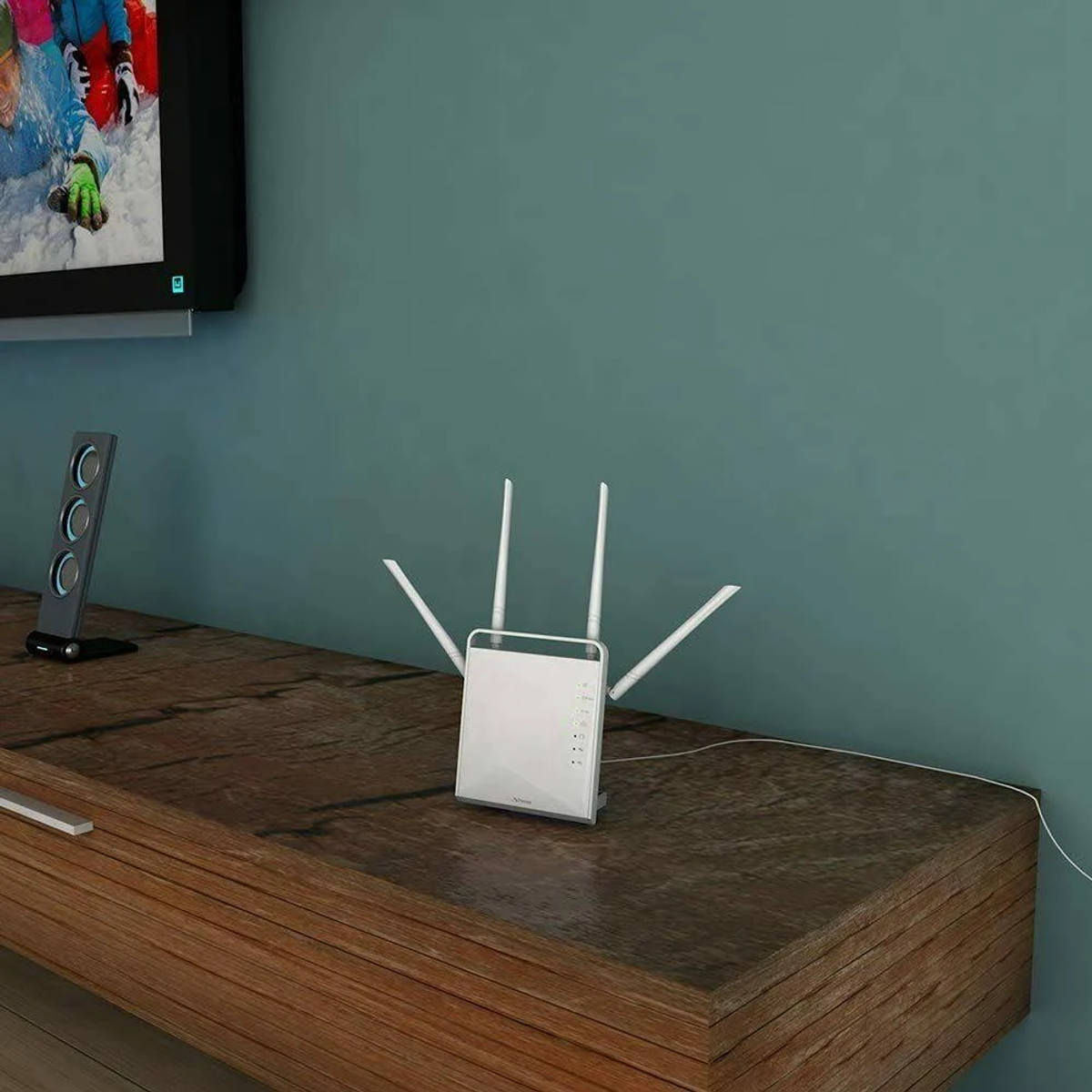 Un router bianco con antenne su un mobile TV in legno accanto a un altoparlante e una parete verde acqua.